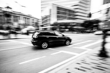 a black and white photo of a car at an intersection in a city